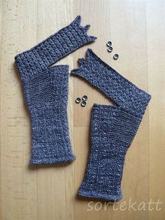 two knitted mittens and one pair of fingerless gloves on a wooden surface