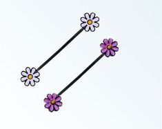 three purple and white flowers with yellow centers on black bobby pin set against a light blue background