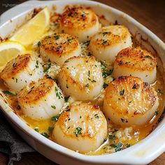 some scallops are in a white dish with lemon wedges