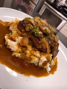 a white plate topped with mashed potatoes and meat covered in gravy on top of a kitchen counter