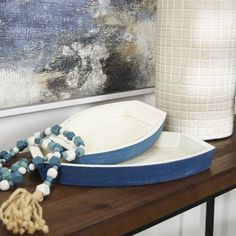 a blue and white boat sitting on top of a wooden table next to a vase