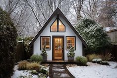 a small white house sitting in the middle of a snow covered yard with trees and bushes