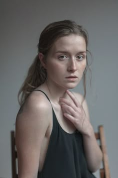 a woman in a black tank top sitting on a wooden chair looking at the camera