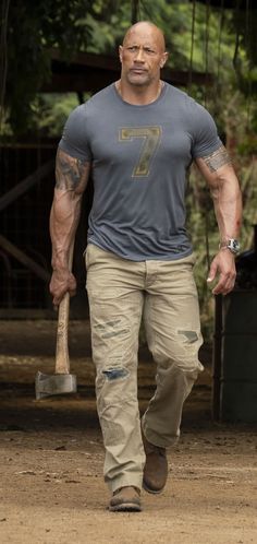 the rock walking with a baseball bat in his hand and wearing a number seven t - shirt