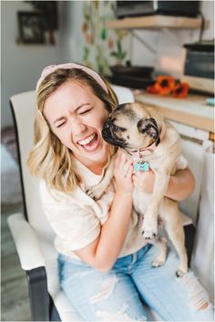 a woman sitting in a chair holding a pug dog and smiling at the camera