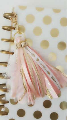 a pink and gold feathered keychain hanging from a binder on a polka dot table