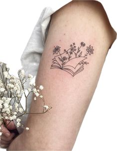 a woman's arm with flowers and an open book tattoo