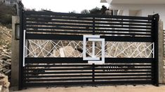 an iron gate with geometric designs on the top and bottom bars, in front of a house