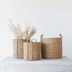 three woven baskets sitting on top of a white table next to each other with feathers in them