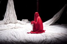 a woman dressed in red sitting on top of a bed covered in white sheeting