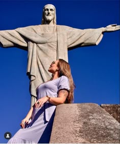 a woman standing in front of the statue of jesus on top of a hill with her eyes closed