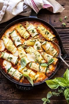 a pan filled with ravioli and cheese on top of a wooden table next to basil leaves