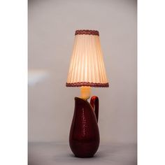 a lamp that is sitting on top of a table with a red vase next to it