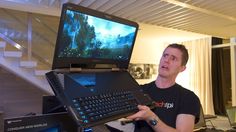 a man holding up a laptop computer with a keyboard on top of it in front of a tv