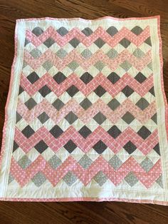 a pink and gray quilt sitting on top of a wooden floor