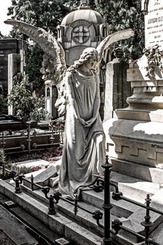 an angel statue is standing in front of a grave with a clock on it's side