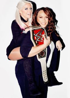 two women are hugging each other while one is holding a wrestling belt in her arms