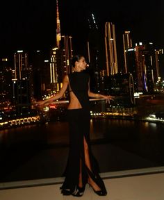 a woman standing on top of a roof in front of a city skyline at night