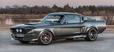 an old mustang muscle car parked in front of a body of water with trees in the background