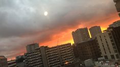 the sun is setting over some buildings in this cityscape, with dark clouds