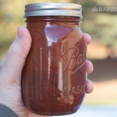 a hand holding a mason jar filled with brown liquid