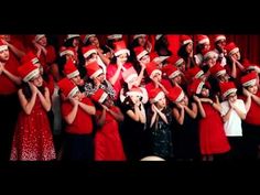 a group of women in red dresses and santa hats singing with their hands up to the side