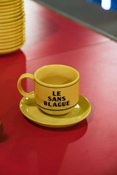 a yellow coffee cup sitting on top of a red table next to stacks of yellow plates