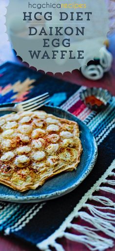 a blue plate topped with waffles on top of a colorful table cloth next to a fork and knife