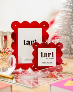 two red frames sitting on top of a table next to a small cup filled with candy