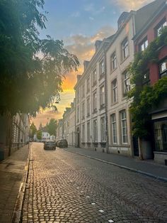 cars are parked on the cobblestone street in front of tall buildings at sunset