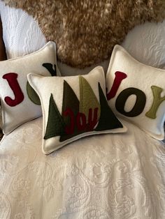 two pillows with the word joy on them sitting on a bed next to a teddy bear