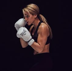 a woman in black shirt and white boxing gloves standing with her hands on her hips