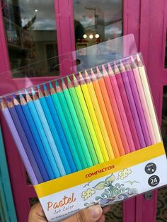 a person holding a box of colored pencils in front of a pink door with the words pastel on it