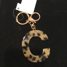 an animal print letter charm hanging from a keychain on a black surface with a white tag attached to it