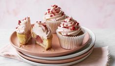 three cupcakes with white frosting and sprinkles on pink plates