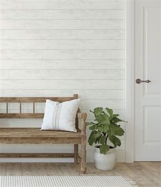 a wooden bench sitting in front of a white wall with a potted plant next to it