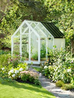 a small white greenhouse in the middle of a garden with flowers and plants around it