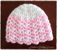 a pink and white crocheted hat sitting on top of a wooden table