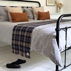 a bed with plaid blankets and slippers on the floor next to a pair of shoes