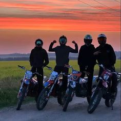 three men standing next to each other on dirt bikes in front of an orange sky