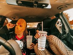 two people sitting in the back seat of a car wearing masks and holding cups with drinks