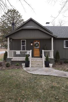 a gray house with white porch and steps leading up to the front door that has a wreath on it