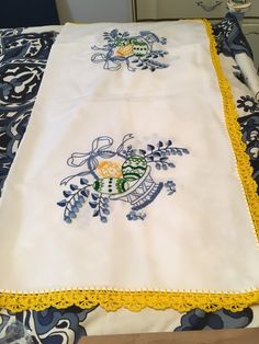 an embroidered tablecloth with yellow trim on a blue and white bedspread in a room