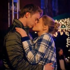 a man and woman kissing in front of christmas lights