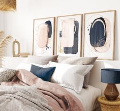 a bed with pillows, blankets and two paintings on the wall above it's headboard