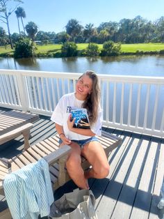 a woman sitting on a bench next to a lake and holding a book in her hands