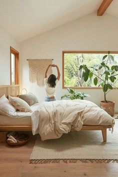 a woman standing on top of a bed in a bedroom next to a large window