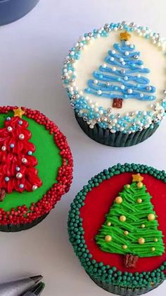 three decorated christmas cupcakes sitting on top of a white table next to scissors