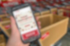 a hand holding a cell phone in front of some cardboard boxes and red lettering on the screen