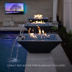 four fire bowls sitting next to a swimming pool filled with water and lit by candles